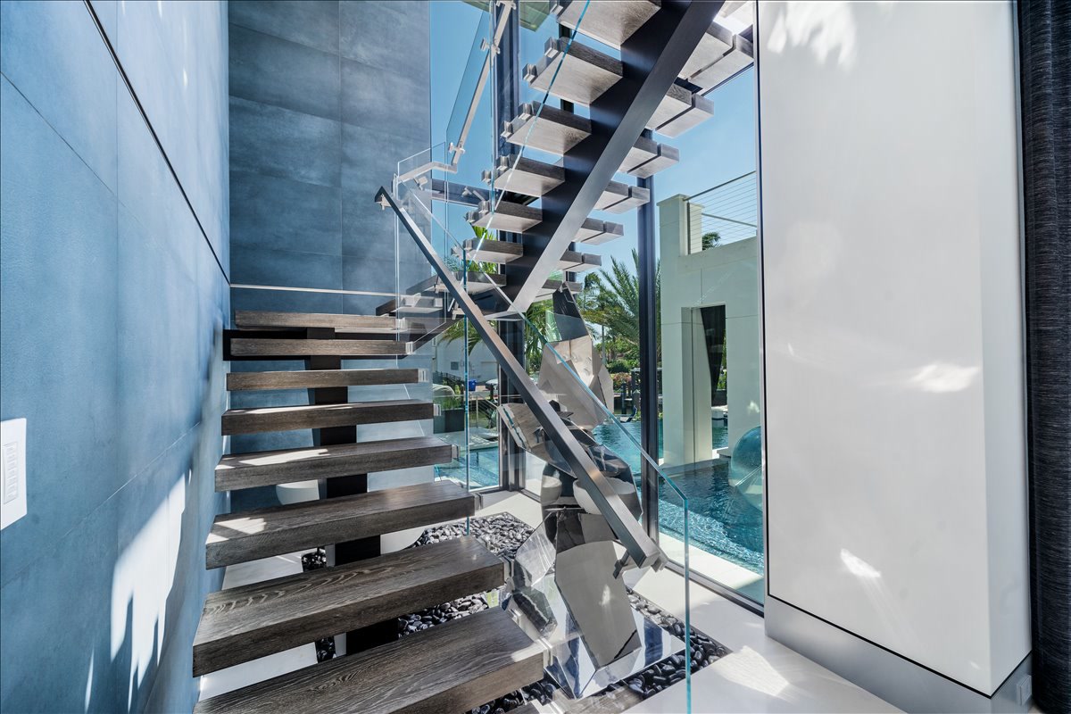 Floating wood and glass staircase beside a blue feature wall
